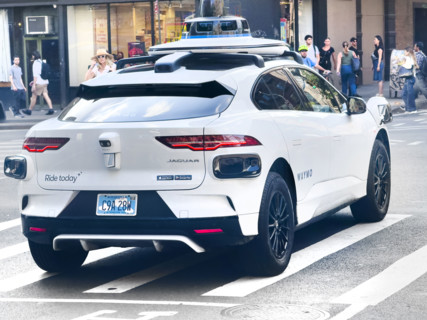 Rear view of Waymo driverless test car, a Jaguar I-PACE electric vehicle and street scene,