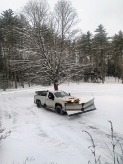 White pickup truck with plow attachment removing snow from residential driveway