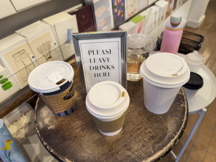 "Please leave drinks here" framed sign on round wood table with paper and plastic cups in retail