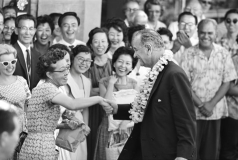 U.S. Vice President Lyndon B. Johnson wearing a lei and shaking a woman's hand, during an overnight