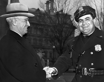U.S. President Harry S. Truman shaking hands with an unidentified police officer while attending