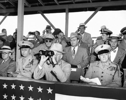 U.S. President Harry S. Truman peering through binoculars, with other dignitaries, watching weapons
