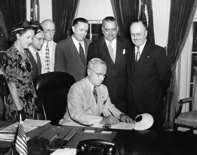 U.S. President Harry S. Truman (seated) in the White House Oval Office signing bill to make