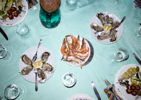 High angle view of dining table featuring plates of oysters and prawns with glasses of water and