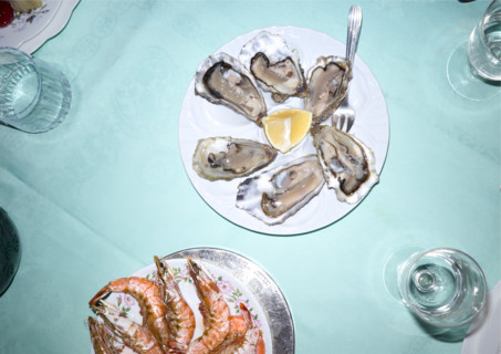 High angle view of dining table featuring plates of oysters and prawns with glasses of water and