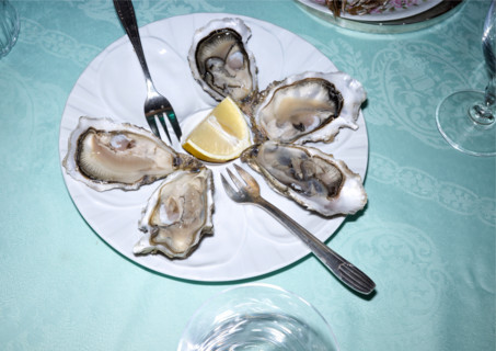 Fresh oysters surrounding a lemon wedge on white plate