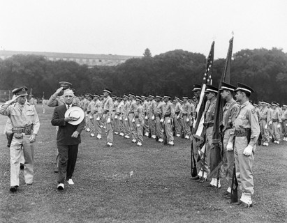 U.S. President Harry S. Truman (in civilian suit and hat) and military officers saluting as they