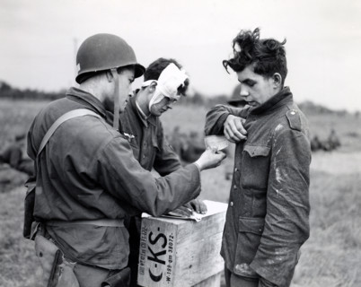 American soldier making out identity tag for young German prisoner of war as another wounded Nazi