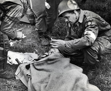 American medical officer, who landed with 82nd Airborne Division, handing lit cigarette to injured