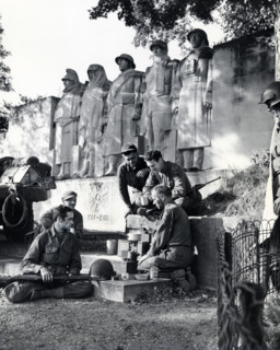 Group of American soldiers cooking dinner on GI stove under World War I memorial, near Verdun,