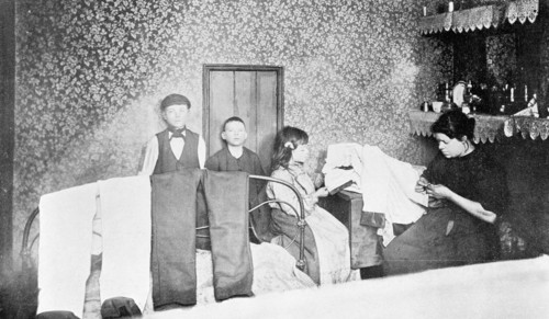 Domestic scene showing a mother with her children finishing trousers, London, c1900. Artist: Unknown