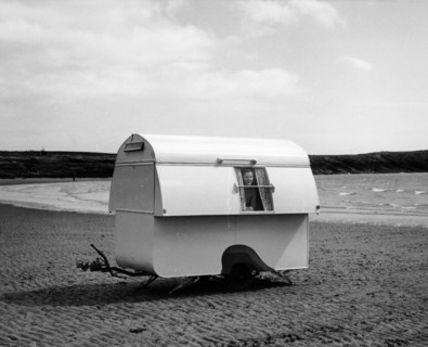 Woman smiling from the window of a trailer caravan on a beach, (c1960s?). Artist: Unknown
