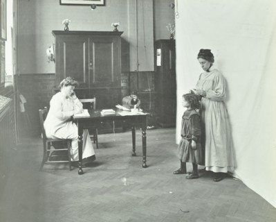 School nurse examining girls' hair for head lice, Chaucer School, London, 1911. Artist: Unknown.