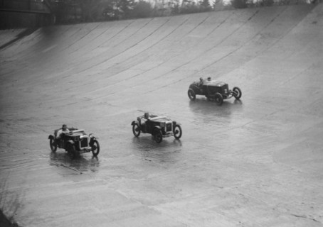 Two Austin 7s and an unidentified car racing at a BARC meeting, Brooklands, Surrey, 1931 Artist: Bill Brunell.