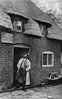 A man smoking a pipe outside a shop, Worcestershire, c1922.Artist: AW Cutler