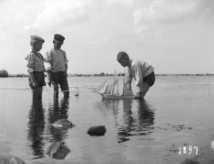 Three boys playing with a model sailing ship, 1897. Artist: Unknown