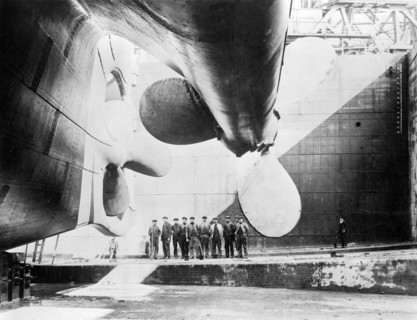 Workmen standing under one of the propellors of the Titanic, 31 May, 1911. Creator: English Photographer (20th Century).