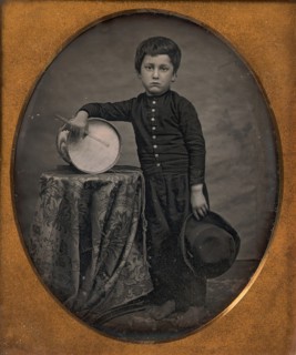 Barefoot Boy Holding Hat and Drum Stick, Leaning Forearm on Child-sized Drum on Table, 1850s.