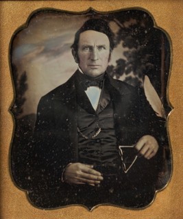 Man Holding Glasses in Front of Painted Outdoor Backdrop, 1850s.