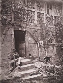 [Man Sitting on Steps of House with Socks Hanging on Nearby Vine to Dry], 1880s.