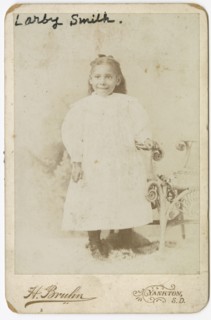 Photograph of Larby Smith standing next to a wicker chair., late 19th century. Creator: Henry Bruhn.