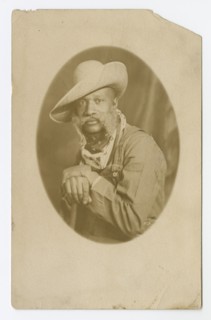 Photographic postcard portrait of a man wearing a hat and overalls, early 20th century. Creator: Unknown.
