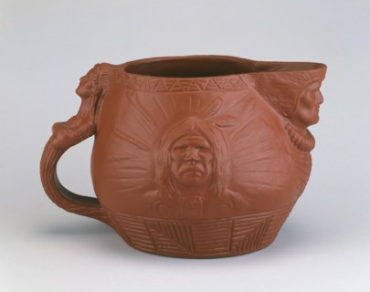 Pitcher, c. 1890.  Earthenware jug with heads of Native Americans on the spout, handle and sides, designed by Edward Kemeys.