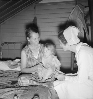 Resident nurse interviews mother and examines sick baby, FSA camp, Farmersville, CA, 1939. Creator: Dorothea Lange.
