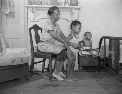 Washington, D.C. Mrs. Ella Watson, a government charwoman dressing her grandchildren.