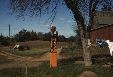 Gas pump with clothesline, barn and horse-drawn wagon in background, between 1941 and 1942. Creator: Unknown.