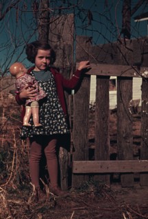 Girl with doll standing by fence, between 1941 and 1942. Creator: Unknown.