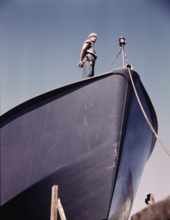 A Coast Guard sentry stands watch over a new torpedo boat under construction at a southern..., 1942. Creator: Howard Hollem.