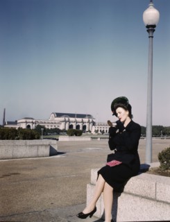 Woman putting on her lipstick in a park with Union Station behind her, Washington, D.C., ca. 1943. Creator: Unknown.