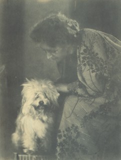 Seated woman petting her white dog, c1900.