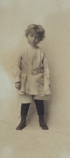 Portrait of a young boy standing in short pants and belted shirt, c1900.
