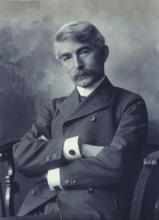 Portrait of man wearing a pinstripe suit seated with his arms crossed, c1900.