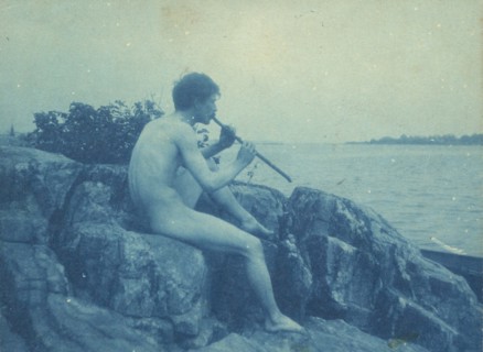 Man posed on rocks, nude, playing pipe (Pan), between 1885 and 1900.