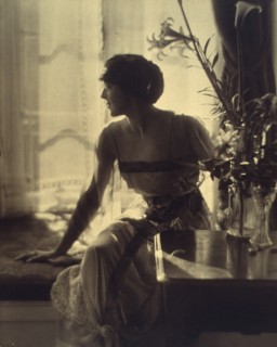 Woman sitting on window seat, looking left, full-length portrait, between 1900 and 1920.