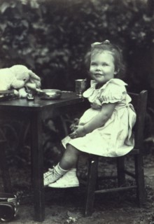 Portrait of a young girl seated at an outdoor table, facing front, between 1940 and 1950.