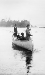 Two Indian guides(?) standing, and two women seated, in canoe, in the Sault Sainte Marie region of Michigan, 1903.