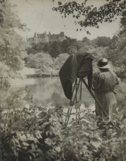 Photographer Frances Benjamin Johnston standing beside her large view camera looking..., c1938. Creator: Unknown.