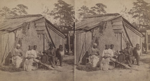 Family group sitting in front of a wooden shack, (1868-1900?). Creator: Unknown.