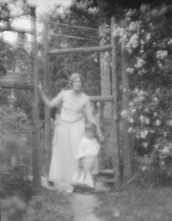 Conroy, Frank, Mrs., and child, standing by a garden gate, 1923 Creator: Arnold Genthe.