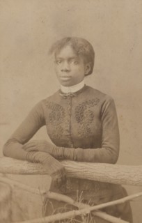 Unidentified young woman wearing gloves, leaning on prop fence, c1880. Creator: H. A. Insley.
