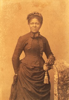 Studio portrait of woman wearing hat and gloves and dress with bustle, c1875. Creator: Unknown.