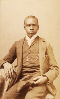 Studio portrait of unidentified seated young man, holding cap, c1880-c1889 . Creator: A. H. Plecker.