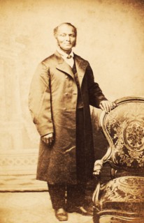 Studio portrait of unidentified man, standing, wearing long coat, c1865. Creator: Sutterley Brothers.
