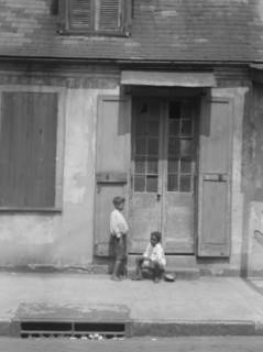 Two children outside a door with shutters in the French Quarter, New Orleans, between 1920 and 1926. Creator: Arnold Genthe.