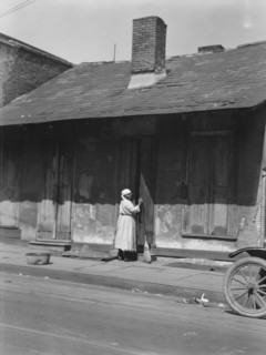 View from across street of a woman with a broom standing in a doorway, New Orleans, c1920-c1926. Creator: Arnold Genthe.