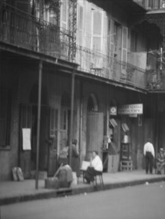 View from across street of people under a covered sidewalk, New Orleans, between 1920 and 1926. Creator: Arnold Genthe.